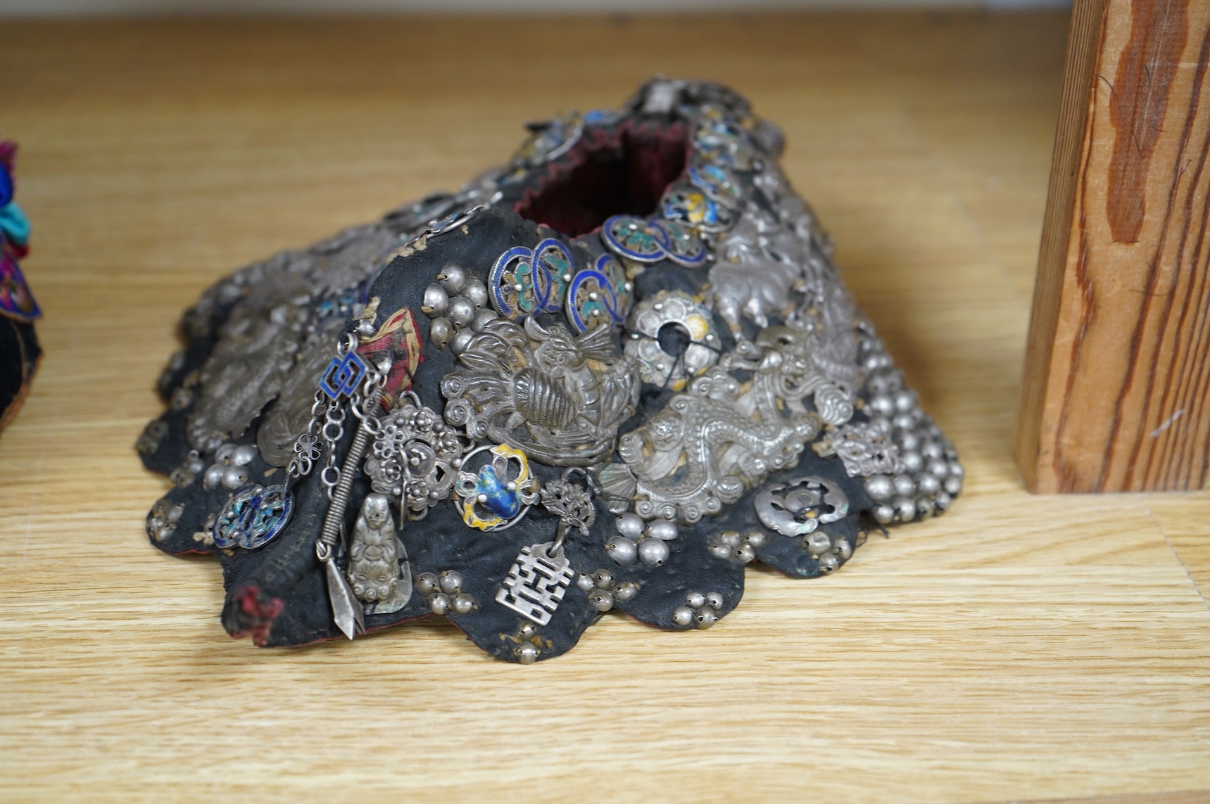 A Chinese Zhuang silver and enamel ceremonial hat, Yunnan Province. The hat heavily covered with auspicious silver and silver enamel charms for good luck and prosperity with a tail/horn shape one side and large silver fl